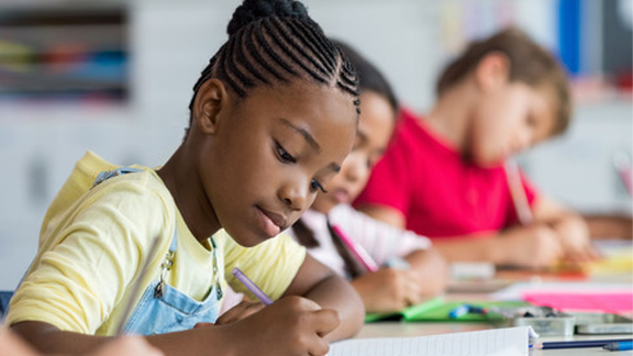 African girl writing in class with blurred background other kids writing 