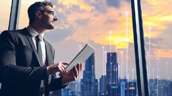 A man looking out of the window with a tablet in hand overlaid with graphics of transmission nodes